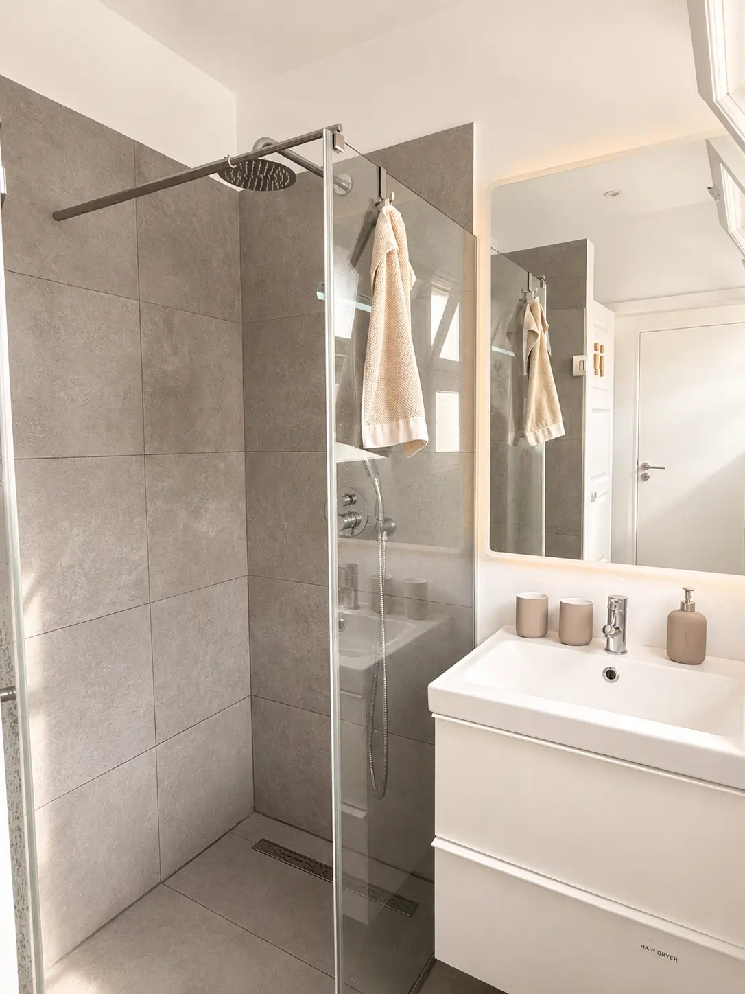 Bright bathroom with a glass walk-in rain shower, towels and a backlit mirror over the sink
