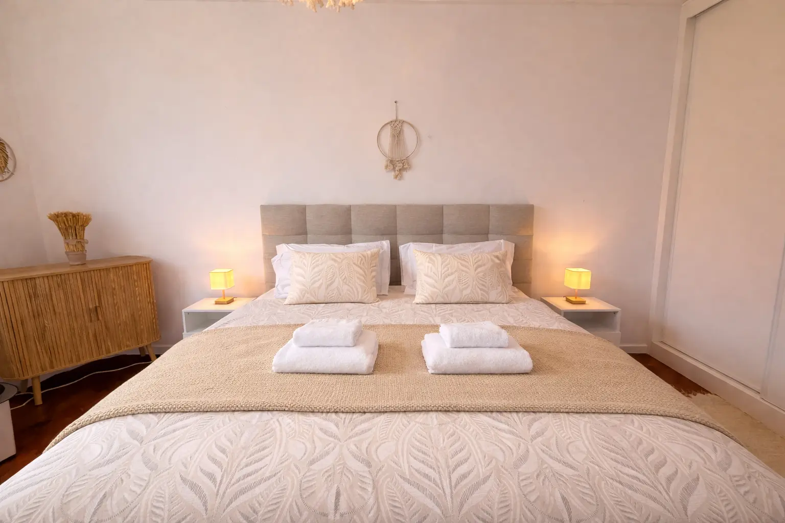 Freshly made double bed with fresh towels, a beige throw and bedside lamps in one of the bedrooms