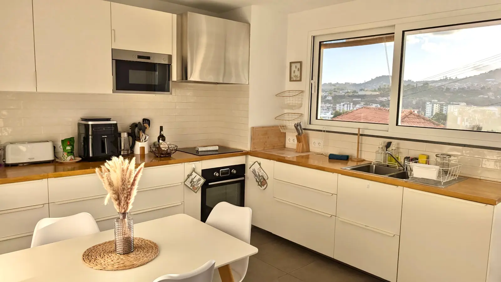 Sunlit white kitchen with wooden worktops, a dining table and views across Funchal