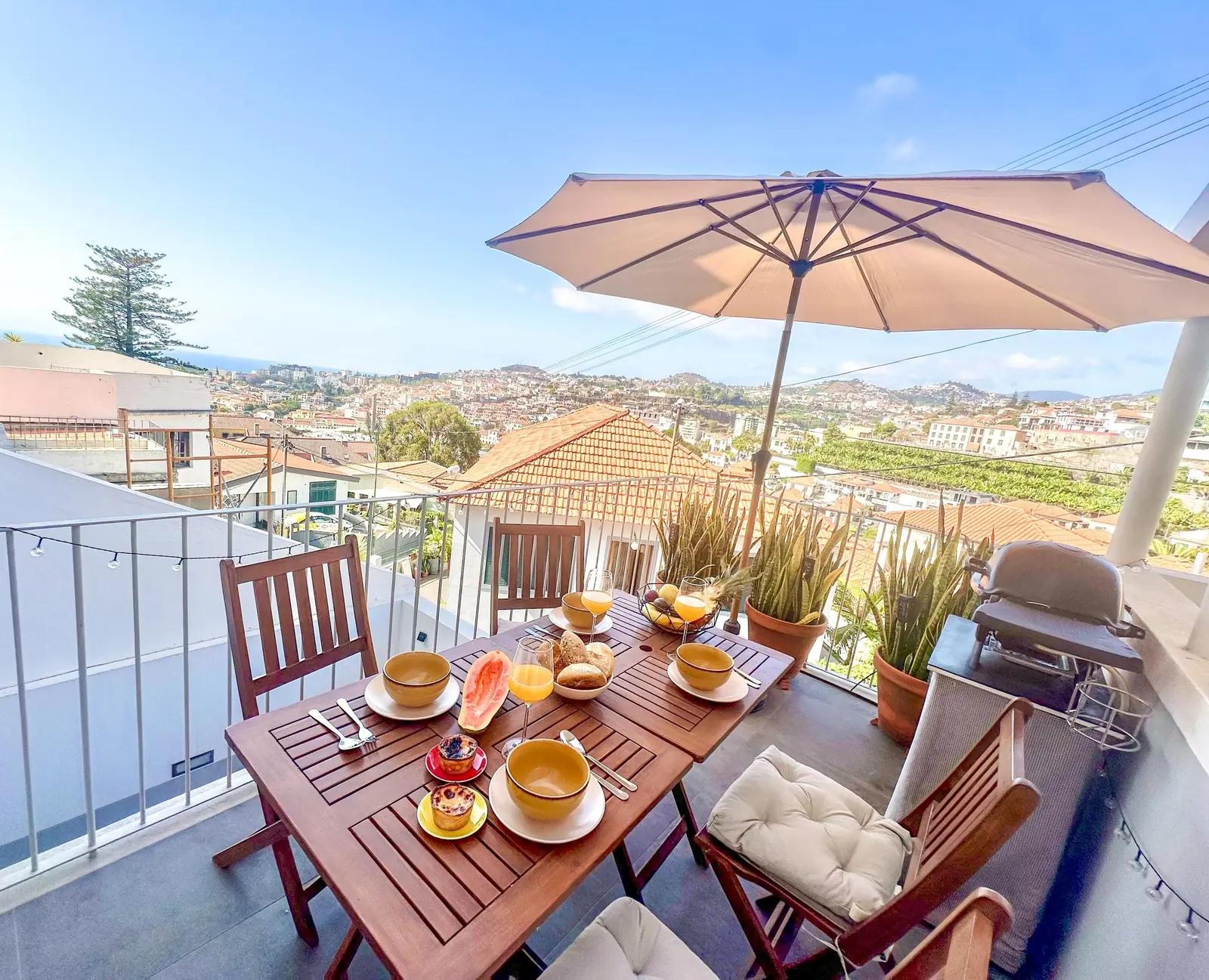 Breakfast table under a parasol on the sunny terrace of Luzia Coliving, overlooking the rooftops of Funchal