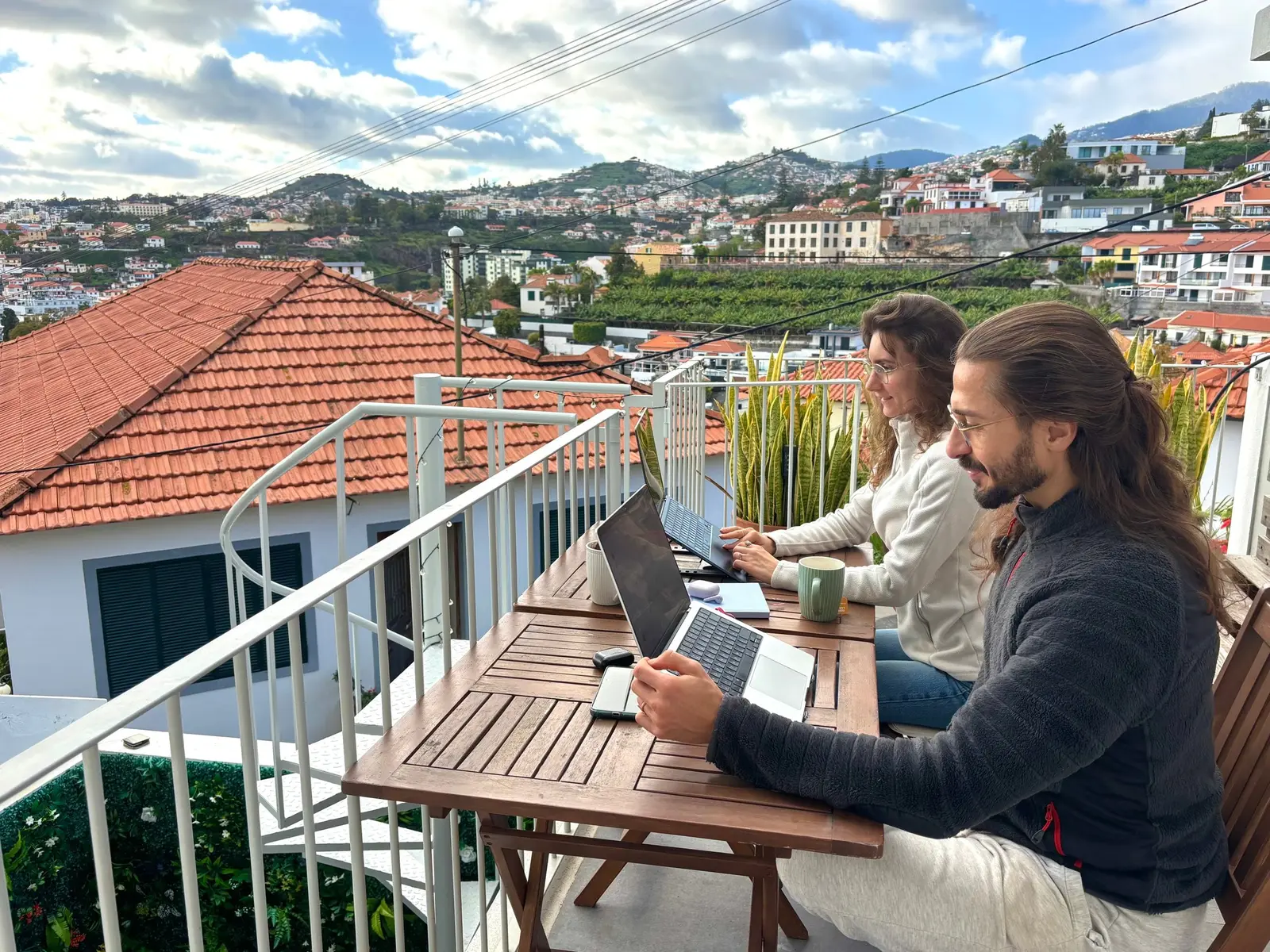 Two residents working on laptops at the terrace table above Funchal