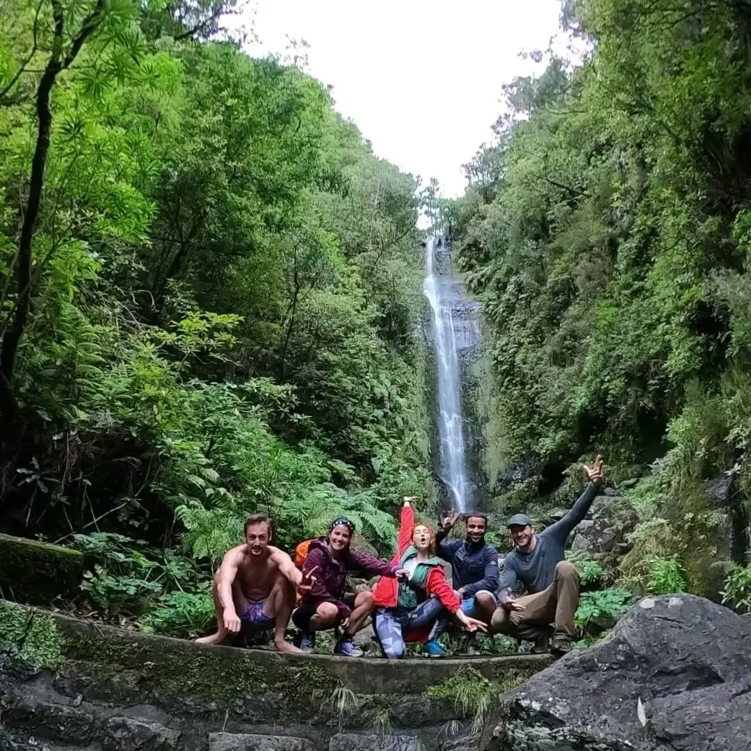 Group of hikers in front of a tall waterfall in a laurel forest